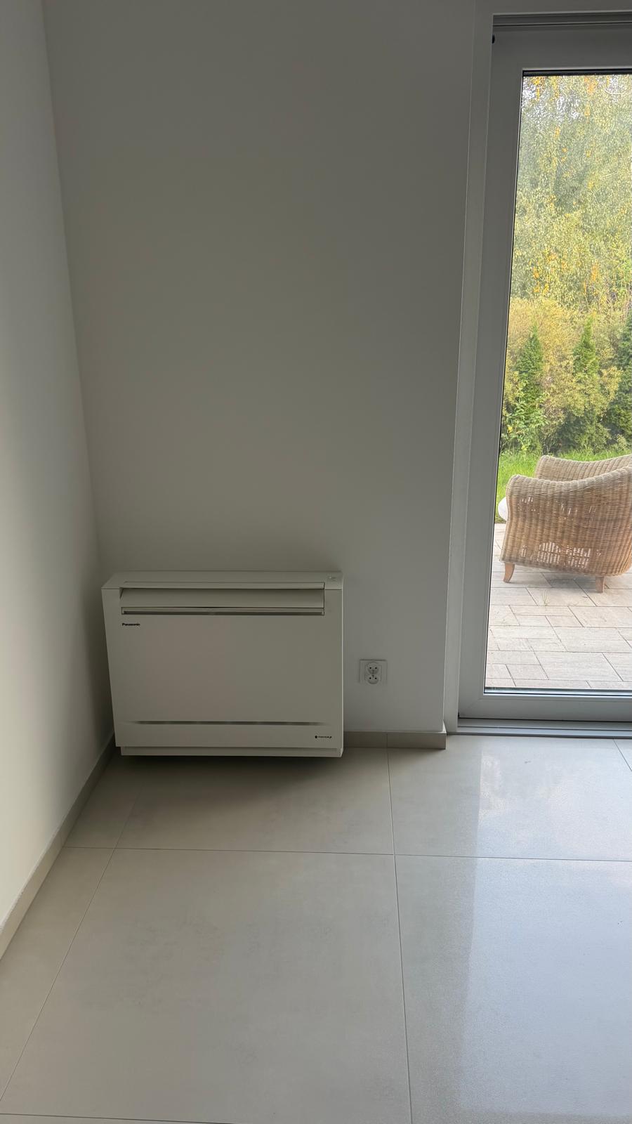 Zdjęcie przedstawia instalatora pracującego na drabinie i bruzdującego ścianę przy użyciu bruzdownicy podłączonej do odkurzacza przemysłowego, podczas prac przygotowawczych pod montaż klimatyzacji/instalacji.