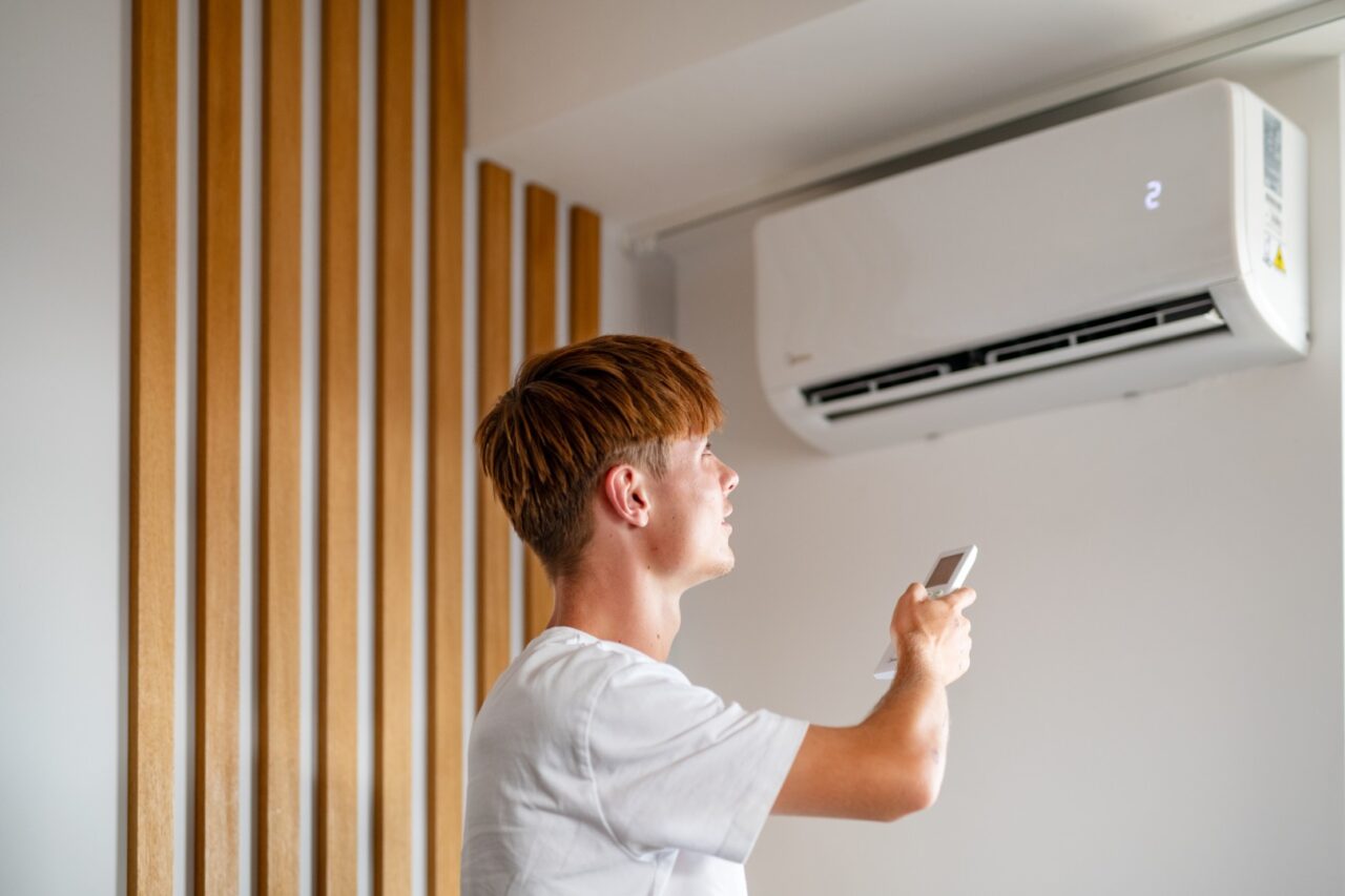 Mężczyzna ustawiający klimatyzację ścienną za pomocą pilota w nowoczesnym wnętrzu